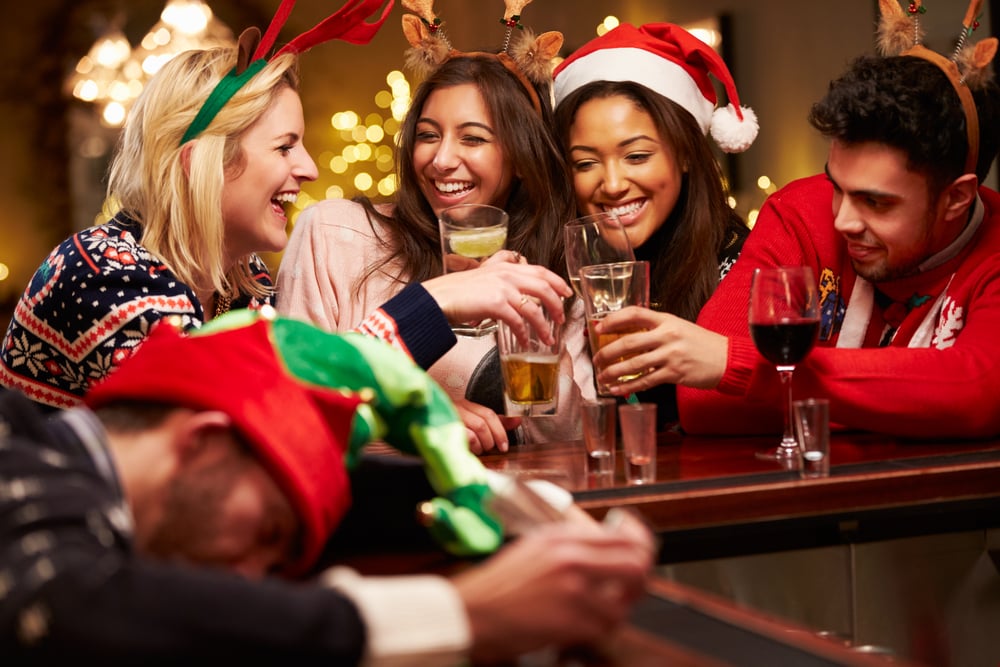 A group of people in ugly sweater and santa hats drinking at a bar during an official bar crawl.