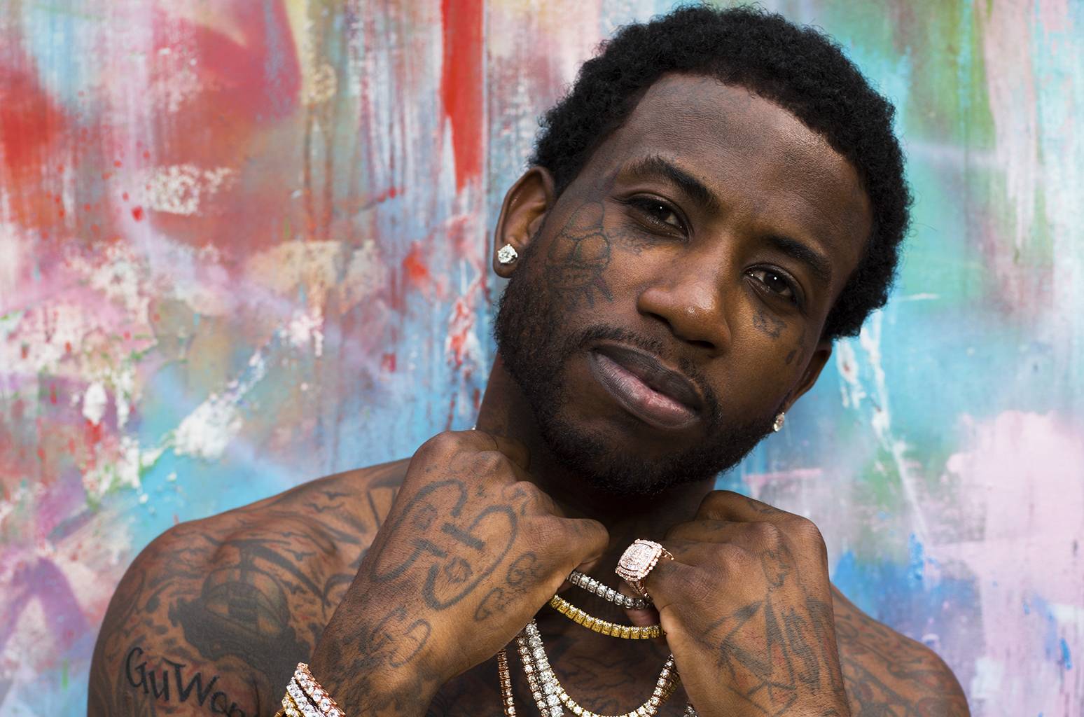 A man with tattoos posing in front of a colorful wall.