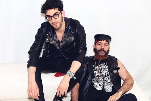 Two men in leather jackets sitting on a white couch.