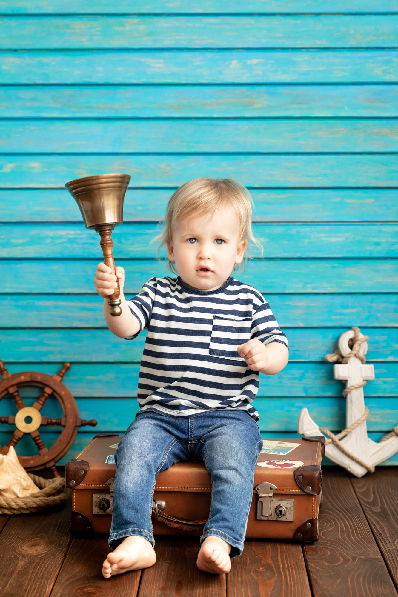 A baby sitting on a suitcase holding a bell amidst November's Fun-Filled Adventures near Harbor Park Garage!