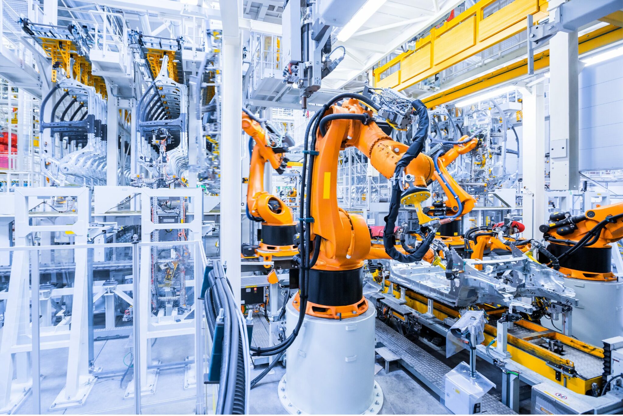 Robotic arms in a modern, automated assembly line work on manufacturing tasks in a bright industrial facility.