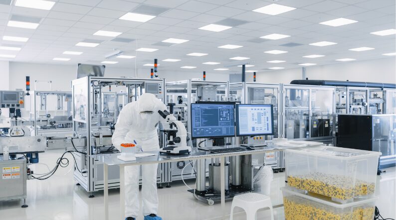 A Halbleiterspezialist in protective gear examines samples with a microscope in a sterile laboratory, surrounded by monitors and cutting-edge equipment.